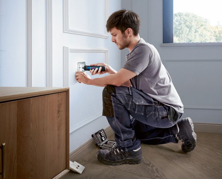 Một người sử dụng tua vít không dây để lắp nắp ổ cắm điện.