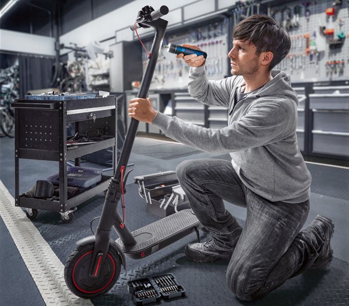 Một người đang sửa xe tay ga điện bằng tua vít không dây trong xưởng.