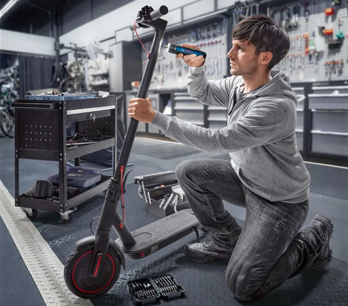 Một người đang sửa xe tay ga điện bằng tua vít không dây trong xưởng.