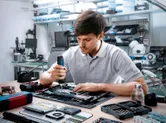 Một người sử dụng tua vít không dây để lắp ráp các linh kiện điện tử trên bàn làm việc.