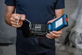 Người đang cầm đèn làm việc LED không dây có pin và tay cầm bằng kim loại.