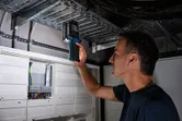 Người đang kiểm tra bảng điện bằng đèn không dây trong phòng tiện ích.