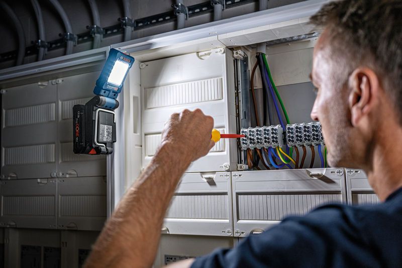 Một người sử dụng tua vít trên bảng điện, gắn đèn không dây để chiếu sáng.