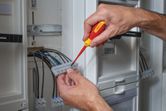 Một người sử dụng tua vít cách điện để siết chặt dây điện trong bảng điện.