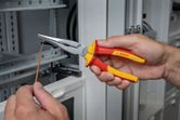 Một người cầm kìm cách điện, định hình một sợi dây gần bảng điện.