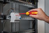 Một người đang siết chặt vít trên một bộ phận điện trong bảng điều khiển.