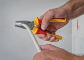 Một người sử dụng kìm cách điện để kẹp và uốn cong một sợi cáp dày màu trắng.