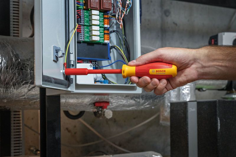 Người sử dụng tua vít cách điện để điều chỉnh hệ thống dây điện trong bảng điện.