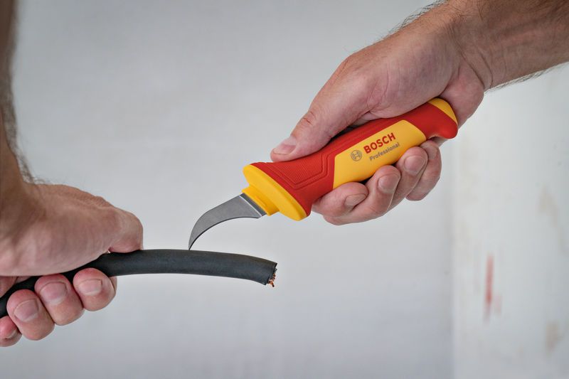 Một người đang dùng dao an toàn cách điện để cắt một sợi cáp dày.