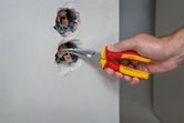 Một người sử dụng kìm mũi cong cách điện để điều chỉnh hệ thống dây điện trong ổ cắm trên tường.
