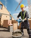 Một người mặc đồ bảo hộ đang trộn xi măng bằng máy khuấy tại một công trường xây dựng.