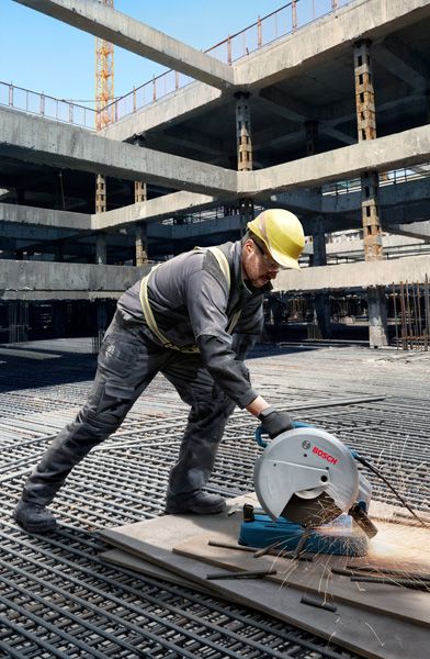 GCO 230 Một người mặc đồ bảo hộ đang dùng cưa cắt ống kim loại tại công trường xây dựng.