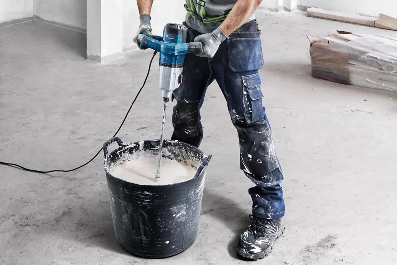 GRW 140 Một người mặc thiết bị an toàn sử dụng cơ chế khuấy để trộn vật liệu trong một chiếc xô lớn.