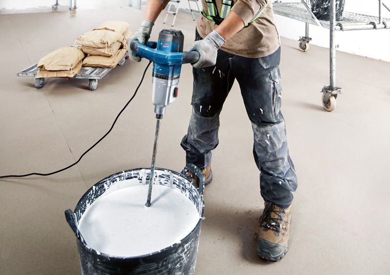 Một người mặc thiết bị an toàn trộn sơn bằng cơ cấu khuấy chạy bằng điện.