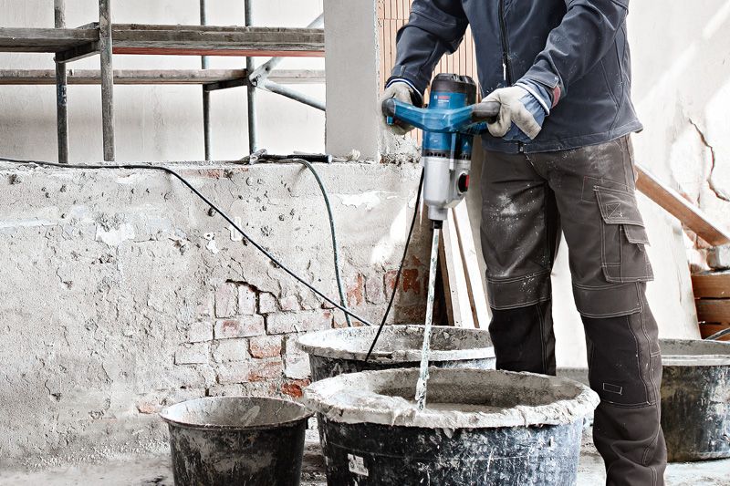 Một người mặc đồ bảo hộ đang trộn vật liệu xây dựng bằng cơ chế khuấy.