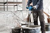 Một người mặc đồ bảo hộ đang trộn vật liệu xây dựng bằng cơ chế khuấy.