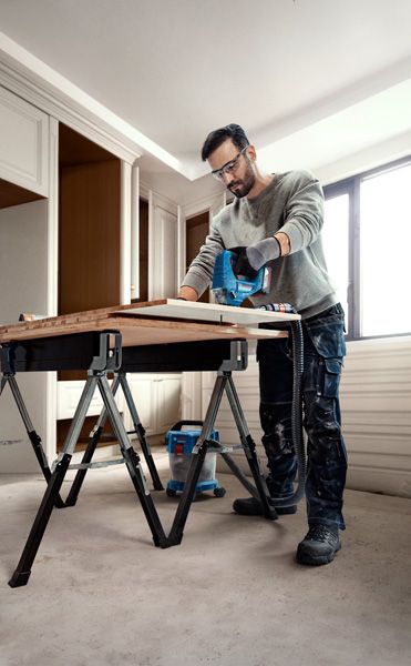 Một người mặc đồ bảo hộ đang sử dụng máy cưa lọng để cắt gỗ trên bàn làm việc.