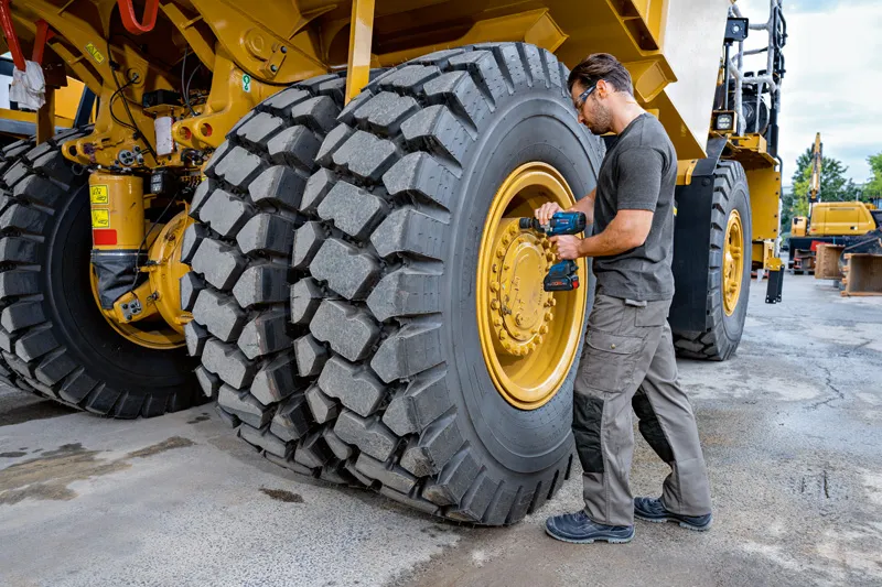 Một người mặc thiết bị an toàn đang sử dụng cờ lê tác động để tháo lốp xe xây dựng cỡ lớn.