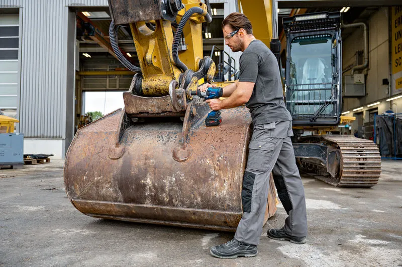 Một người mặc thiết bị an toàn đang sử dụng cờ lê tác động trên máy móc xây dựng hạng nặng.