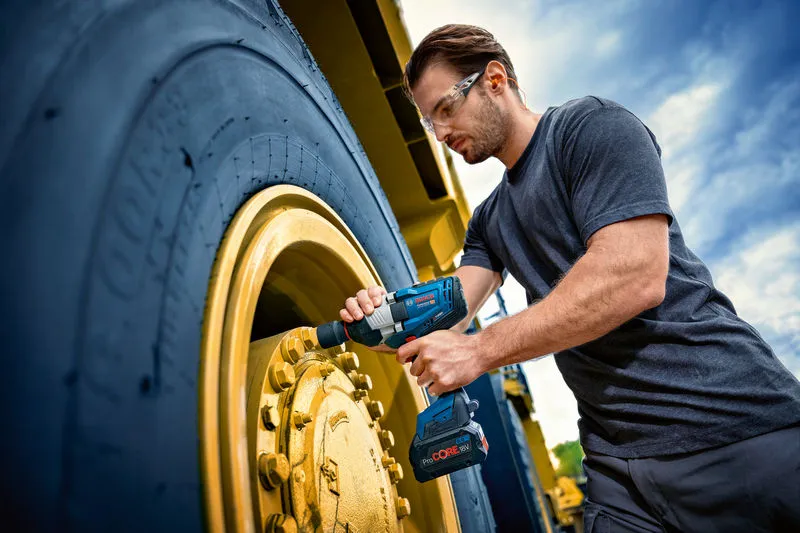 Một người mặc thiết bị an toàn đang sử dụng cờ lê tác động vào bánh xe của một chiếc xe lớn.