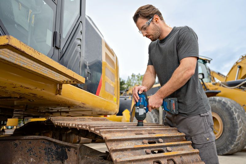 Một người mặc thiết bị an toàn đang sử dụng cờ lê tác động không dây trên đường ray của máy xúc.