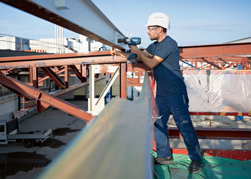 Một người mặc thiết bị an toàn đang sử dụng cờ lê tác động không dây trên một thanh thép.