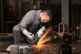 Một người mặc đồ bảo hộ đang mài bề mặt kim loại bằng máy mài góc.