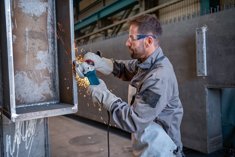 Một người mặc đồ bảo hộ sẽ mài kim loại bằng máy mài góc, tạo ra tia lửa.