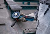Một người mặc đồ bảo hộ đang cầm máy mài góc trong môi trường công nghiệp.
