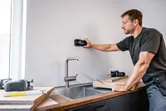Một người đang quét tường bếp phía trên bồn rửa bằng công cụ dò tìm kỹ thuật số.