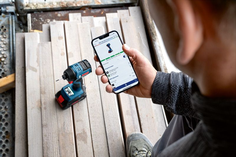 Một người đang kiểm tra các tính năng ứng dụng của dụng cụ điện trên điện thoại thông minh gần máy khoan không dây.