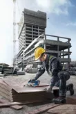 Một người mặc đồ bảo hộ đang cắt ván ép tại công trường xây dựng bằng cưa không dây.