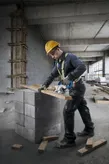 Một người mặc đồ bảo hộ đang dùng cưa tròn để cắt gỗ trên các khối bê tông.
