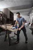 Một người mặc đồ bảo hộ đang cắt gỗ bằng máy cưa tròn không dây trong xưởng.