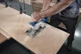 Một người đang cắt ván ép bằng máy cưa tròn trong một xưởng chế biến gỗ.