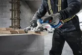 Một người mặc đồ bảo hộ đang cắt gỗ bằng máy cưa tròn tại công trường xây dựng.