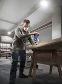 Một người mặc thiết bị an toàn sử dụng máy phay ở mép bàn gỗ.