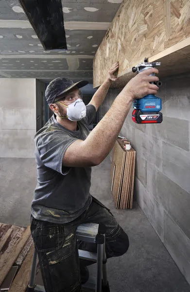 Một người mặc đồ bảo hộ đang sử dụng máy phay trên kệ gỗ.