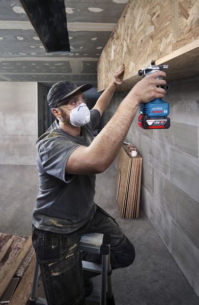 Một người mặc đồ bảo hộ đang sử dụng máy phay trên kệ gỗ.