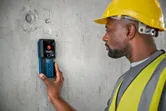 Một người mặc thiết bị an toàn sử dụng máy dò để quét bức tường bê tông.