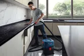 Một người mặc đồ bảo hộ đang vệ sinh ngăn kéo bếp bằng máy hút bụi ướt.
