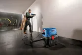 Một người mặc đồ bảo hộ khoan vào tường, máy hút bụi ướt-khô được kết nối ở gần đó.