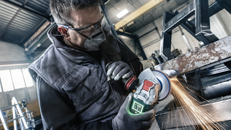 Một người mặc đồ bảo hộ mài một thanh kim loại, tạo ra tia lửa sáng.