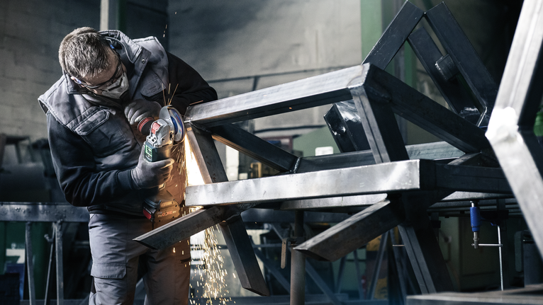 Một người mặc đồ bảo hộ mài khung kim loại, tạo ra tia lửa.