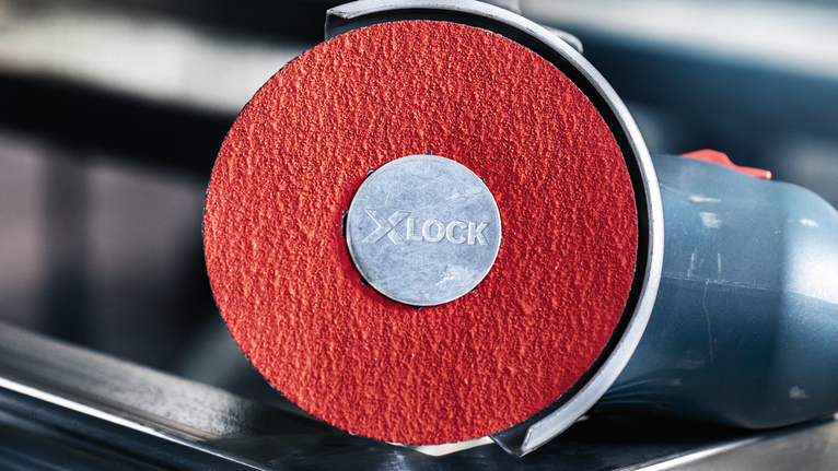 Nhám đĩa PRO R780 X-Lock, 125 mm, G36 Cận cảnh máy mài góc có đĩa mài màu đỏ nằm trên kim loại.