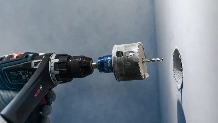 Người đeo thiết bị an toàn khoan một lỗ tròn vào tường.