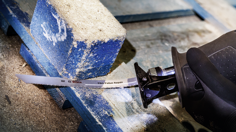 Người mặc đồ bảo hộ đang cắt một tấm pallet gỗ bằng máy cưa lọng.