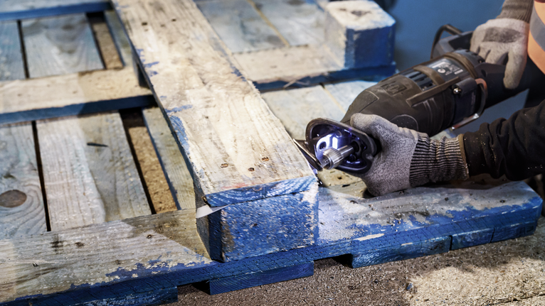 Người mặc đồ bảo hộ đang cắt một tấm pallet gỗ bằng máy cưa lọng.