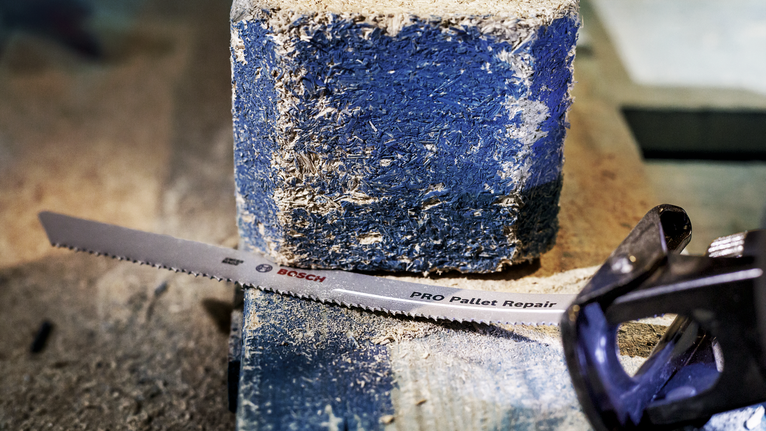 Lưỡi cưa qua lại nằm trên một khối gỗ pallet bụi bặm.