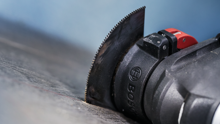 Dụng cụ đa năng dao động có lưỡi dao thẳng cắt vào bề mặt tối.